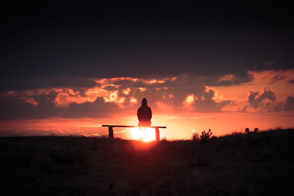 Silhouette of a person sitting alone on a bench at sunset