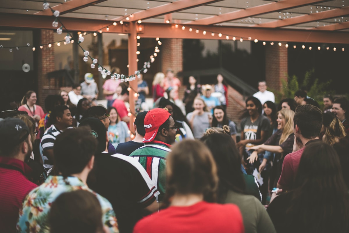 A crowd of people gathered close together at an outdoor evening gathering under string lights