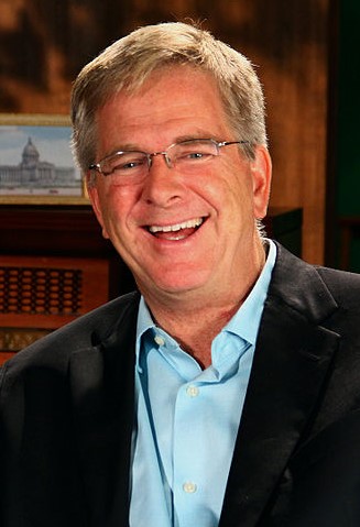 Rick Steves, smiling portrait in a dark blazer and light blue shirt.