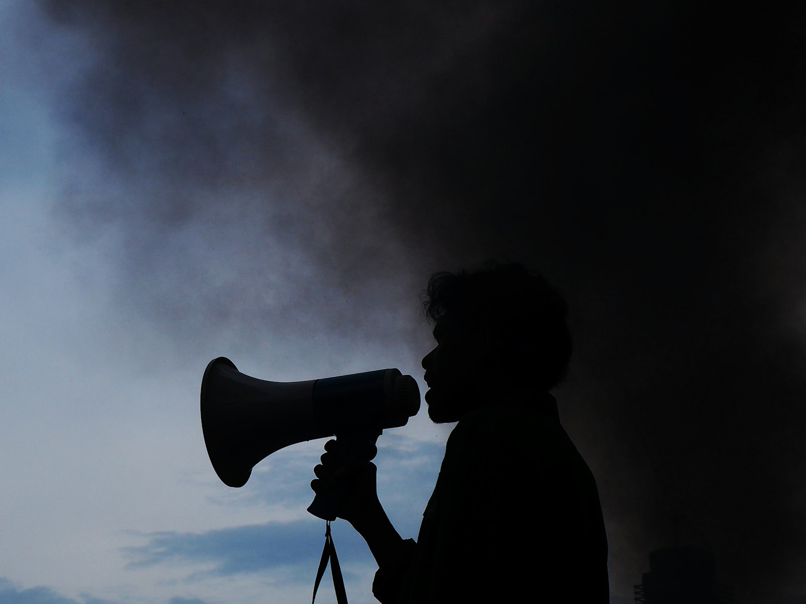 Silhouette of a person shouting into a megaphone against a smoke-hazed sky