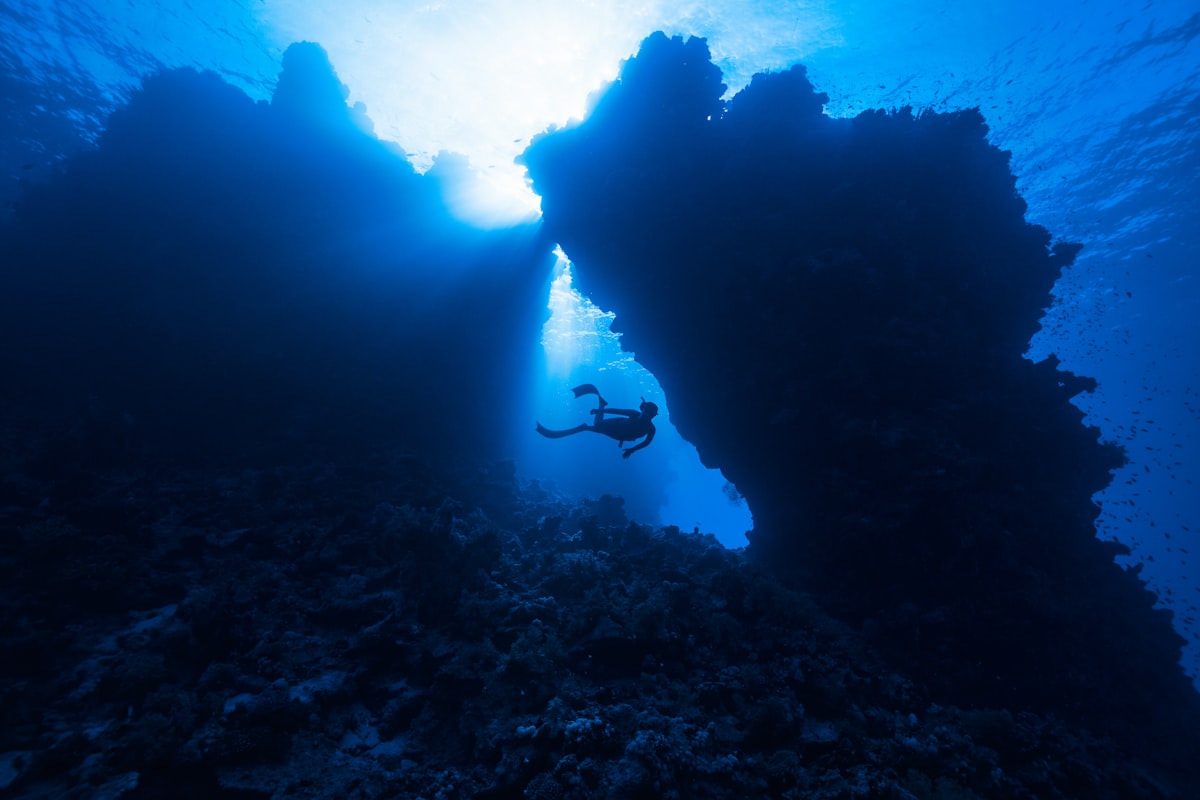 A lone diver moving through deep water beside a submerged rock formation