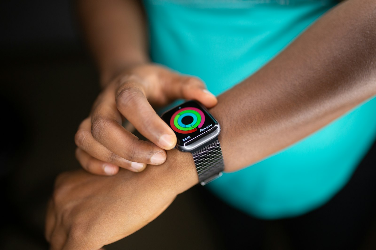 A close-up of a smartwatch on a wrist showing completed activity rings, the wearer's other hand touching the screen